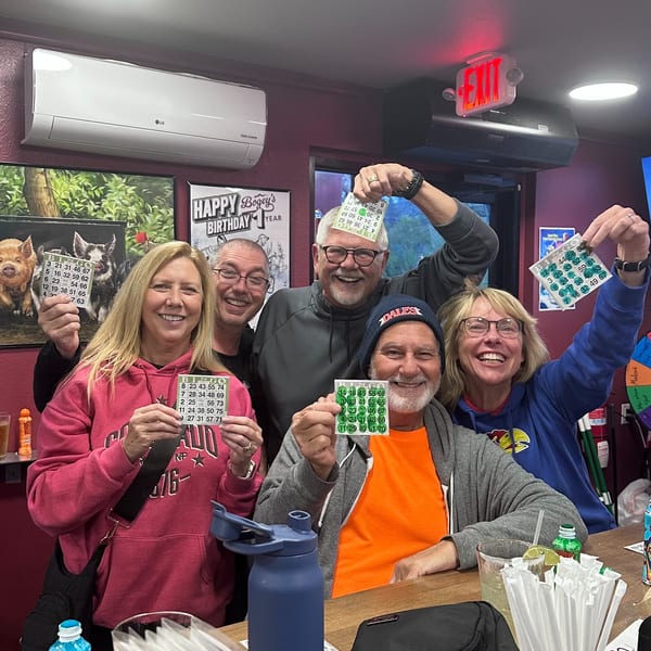 Five smiling adults at a bar holding up Bingo cards, celebrating a birthday.