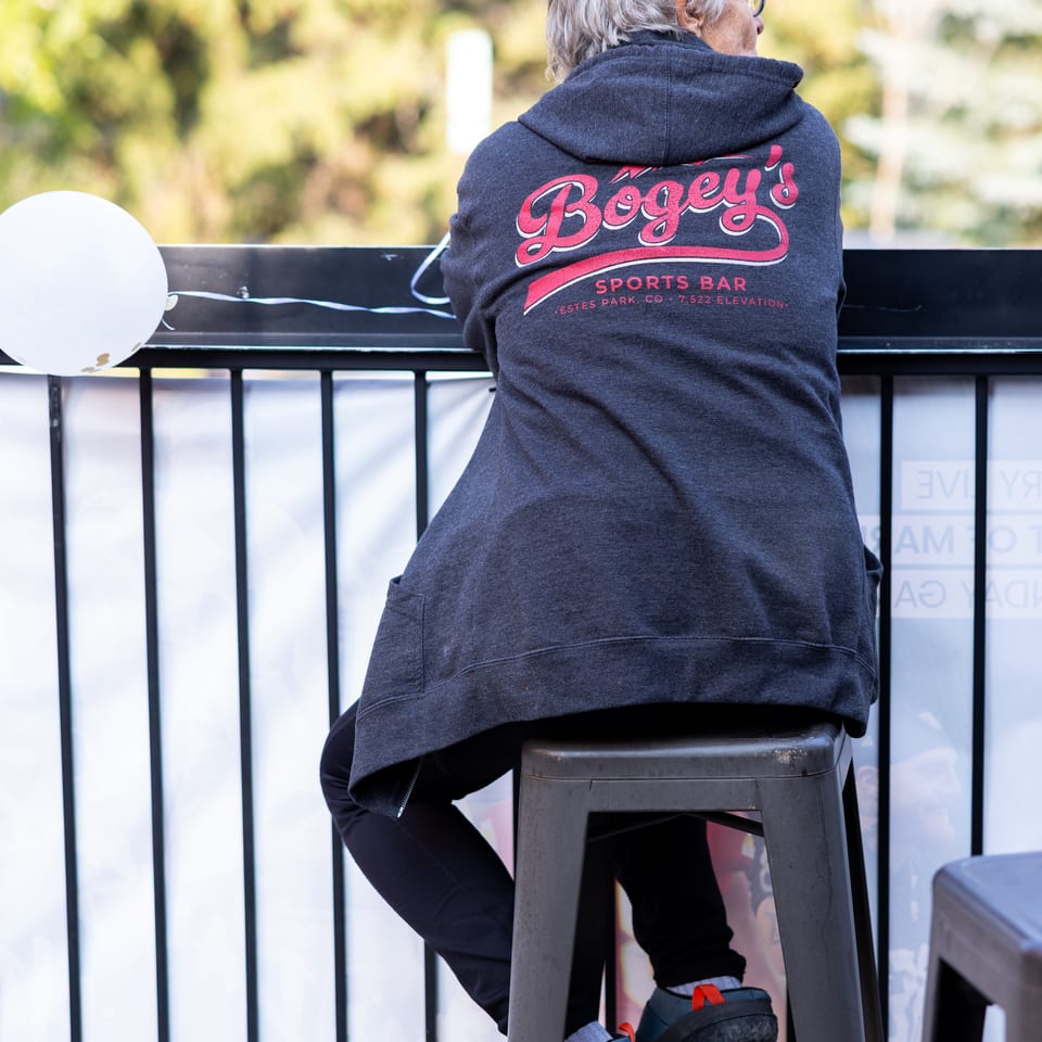 Person in a "Bogey's Sports Bar" hoodie sits on a stool, looking out over a railing.