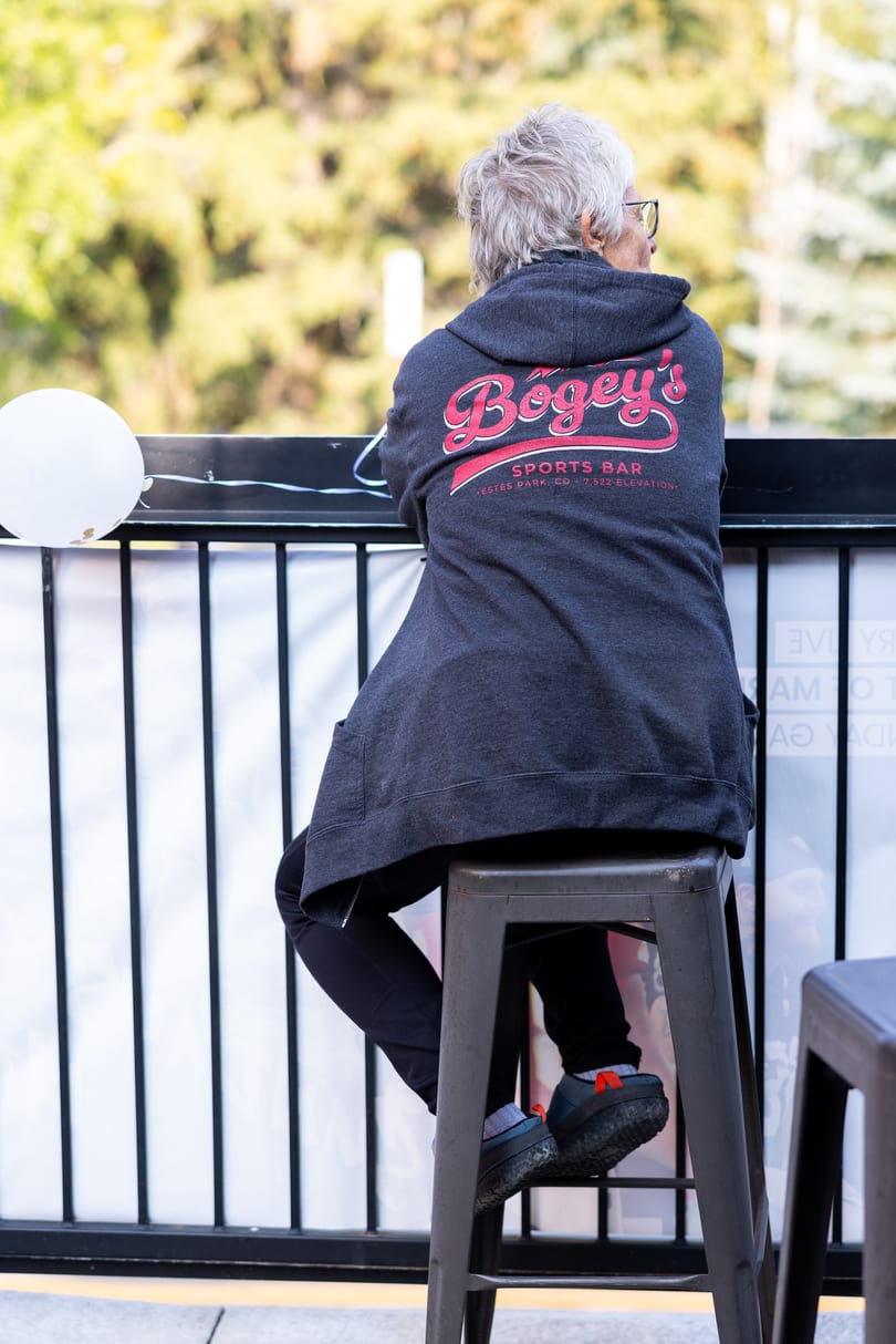 Person in a "Bogey's Sports Bar" hoodie sits on a stool, looking out over a railing.