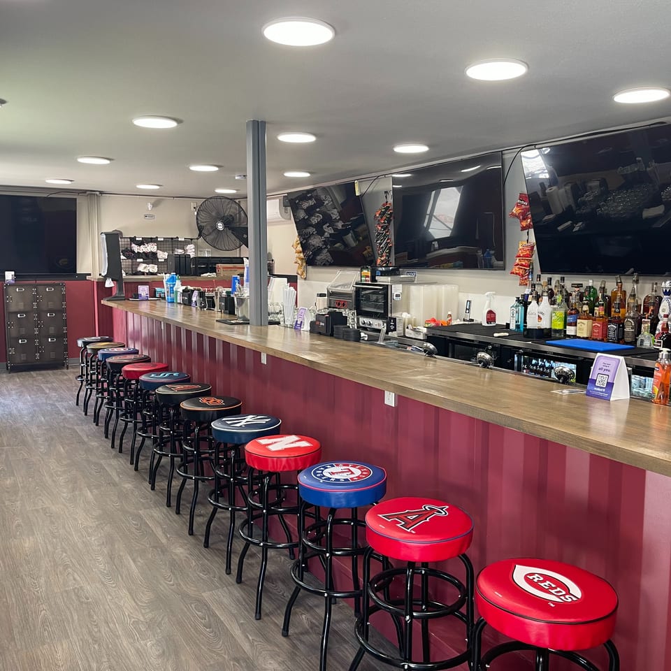 Interior view of a sports bar with a long counter, many team logo bar stools, and TVs.