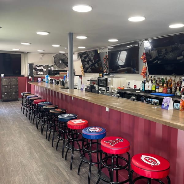 Long bar with red corrugated siding, numerous stools with sports team logos, and multiple TVs.