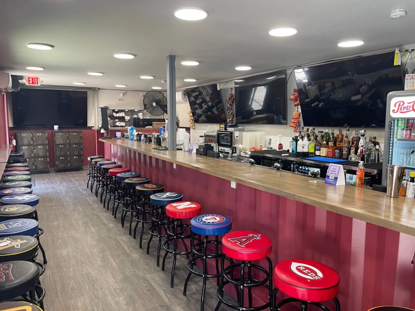 Long bar with red corrugated siding, numerous stools with sports team logos, and multiple TVs.