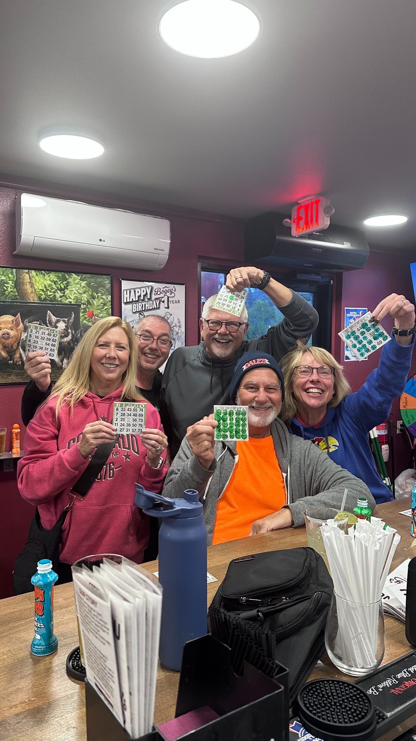 Cheerful group of five people holding bingo cards, celebrating at a restaurant bar.